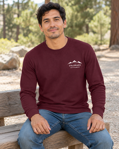 Illustrative lifestyle mockup: man wearing the Maroon Colorado Mountain Waffle Long Sleeve on a trailhead bench, showing the small white left-chest mountain logo.