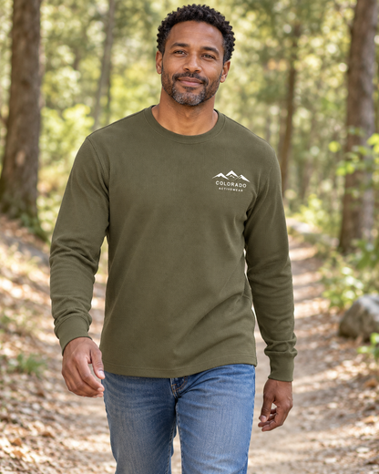 Illustrative lifestyle mockup: man wearing the Military Green Colorado Mountain Waffle Long Sleeve on a wooded path, showing its small white left-chest mountain logo.