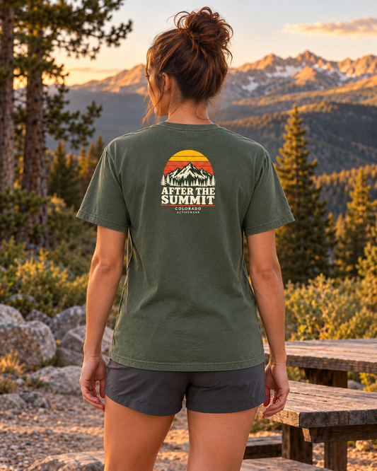 Woman wearing the After the Summit Heavyweight Tee in Moss outdoors, showing the compact retro sunset and mountain back graphic.