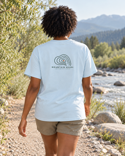 Chambray Mountain Hours Contour Tee on a woman walking beside a river, showing the compact contour-line back graphic; illustrative lifestyle mockup.